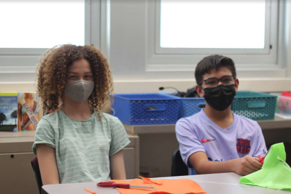 2 students smiling in masks at desk