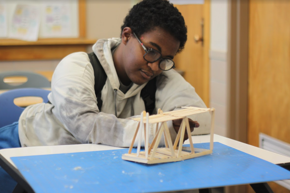 Student working on a bridge built in popsicle sticks
